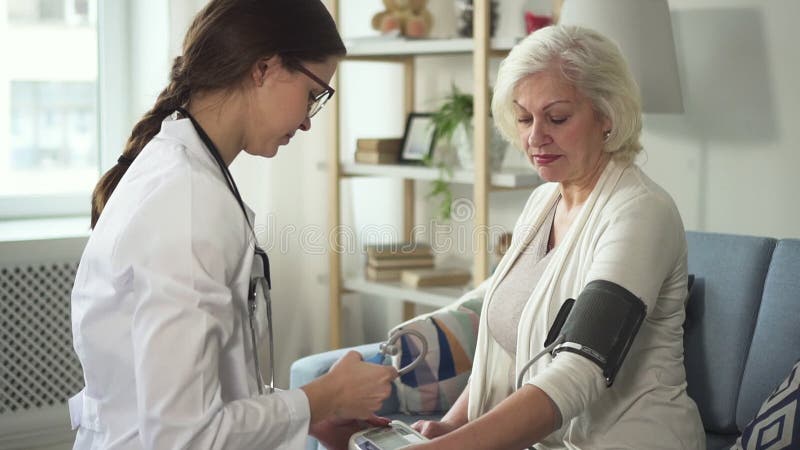 Il medico è misurante e controllante la pressione paziente senior facendo uso dello stetoscopio