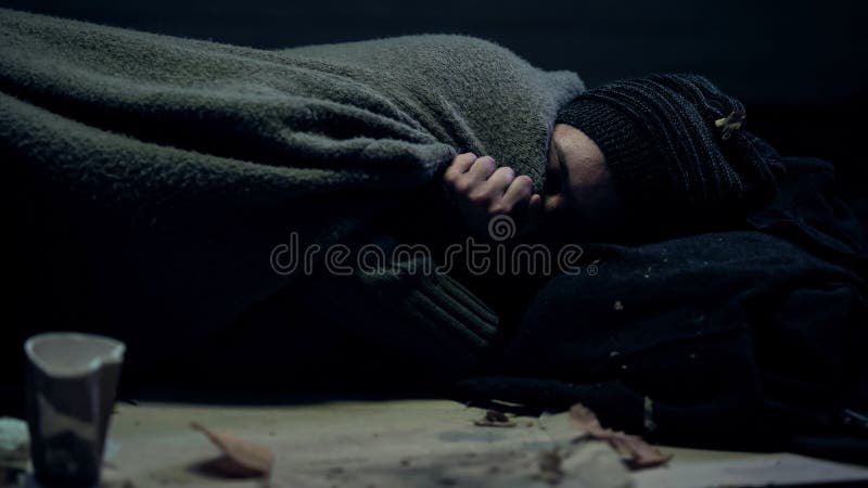 Il mendicante povero ha coperto la coperta sporca che dorme sul freddo ritenente della via, l'essere senza tetto