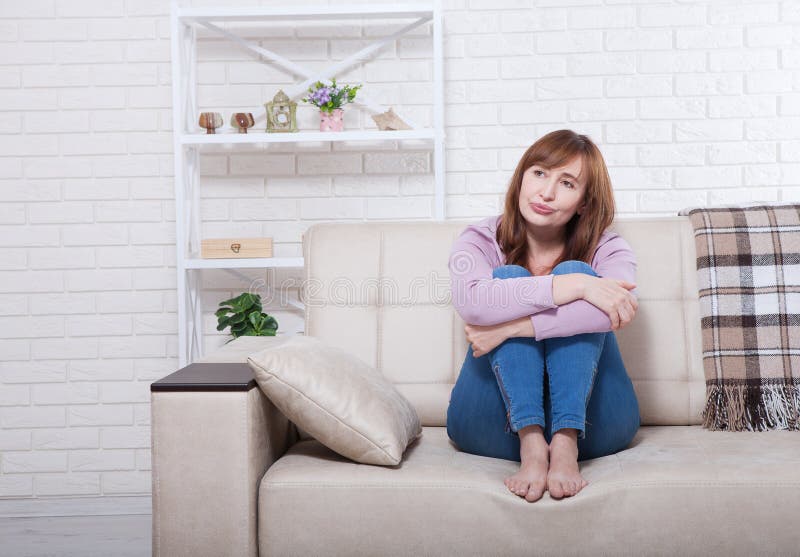 Il mezzo depresso e triste ha invecchiato la donna che si siede con le ginocchia premute sul letto, la vettura, sofà a casa Copi immagini stock Il mezzo depresso e triste ha invecchiato la donna che si siede con le ginocchia premute sul letto, la vettura, sofà a casa Copi immagini stock