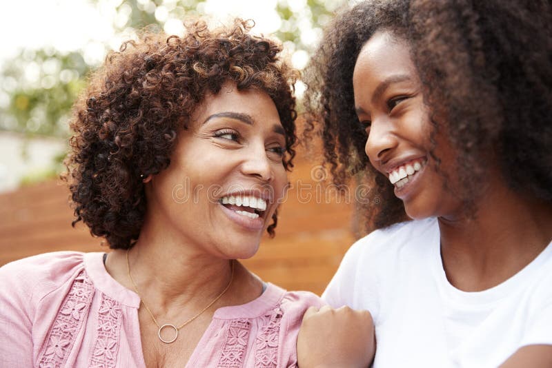 Il mezzo ha invecchiato la mummia afroamericana e la figlia teenager che sorridono ad a vicenda immagini stock libere da diritti Il mezzo ha invecchiato la mummia afroamericana e la figlia teenager che sorridono ad a vicenda immagini stock libere da diritti