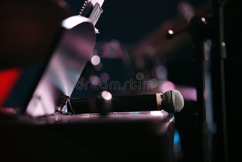 Il microfono è posizionato sul piano. Il microfono viene posizionato sulla copertina del piano con un supporto per note sullo sfondo di luci astratte su una parete nera Prestazione pubblica sul palcoscenico