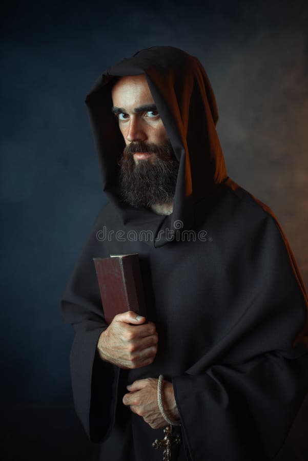 Medieval monk in robe holds spellbook in hands, black background, secret ritual. Mysterious friar in dark cape. Mystery and spirituality. Medieval monk in robe holds spellbook in hands, black background, secret ritual. Mysterious friar in dark cape. Mystery and spirituality