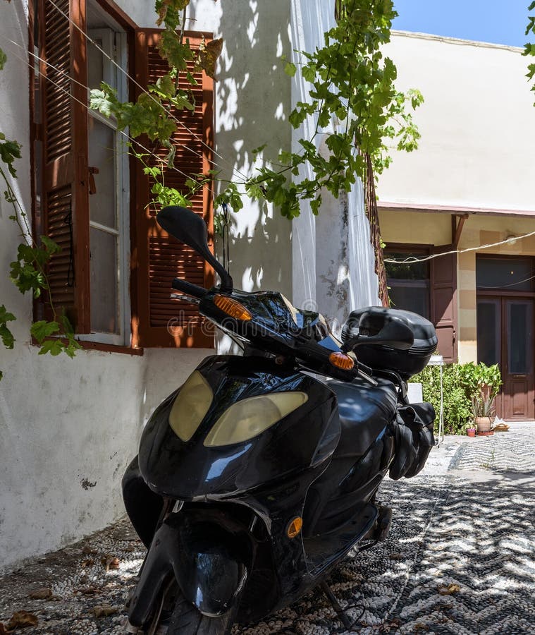 Il motorino della motocicletta è parcheggiato vicino al cespuglio porpora di bougainvelia alla via della città di Rodi sull'isola fotografia stock Il motorino della motocicletta è parcheggiato vicino al cespuglio porpora di bougainvelia alla via della città di Rodi sull'isola fotografia stock
