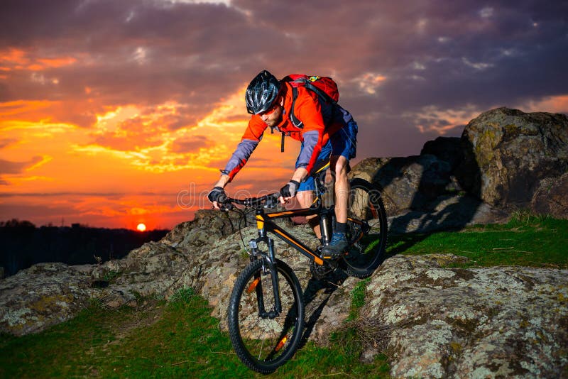Il mountain bike di guida del ciclista giù balza Rocky Hill al bello tramonto Sport e concetto estremi di avventura