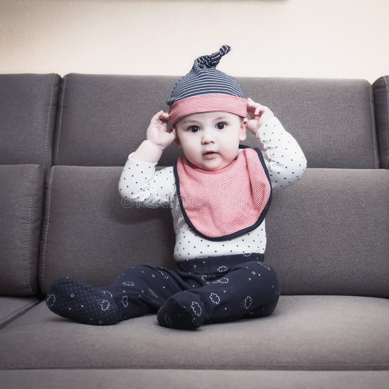 Il neonato caucasico weared la busbana francese che si siede sul sofà a casa fotografia stock Il neonato caucasico weared la busbana francese che si siede sul sofà a casa fotografia stock