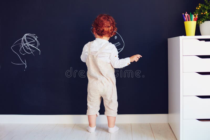 Il neonato sveglio della testarossa che attinge il gesso mura a casa fotografie stock libere da diritti Il neonato sveglio della testarossa che attinge il gesso mura a casa fotografie stock libere da diritti