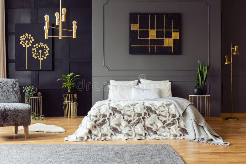 Il nero e manifesto dell'oro sulla parete grigia sopra il letto nell'interno della camera da letto con le piante e la poltrona Fo fotografia stock libera da diritti