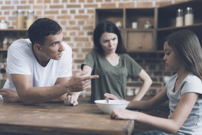 Il padre sta parlando con sua figlia triste, che sta sedendosi alla tavola e non vuole mangiare la sua prima colazione immagine stock Il padre sta parlando con sua figlia triste, che sta sedendosi alla tavola e non vuole mangiare la sua prima colazione immagine stock