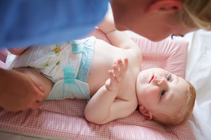 Il pannolino del figlio cambiante del bambino della madre come si trova sulla stuoia immagini stock libere da diritti Il pannolino del figlio cambiante del bambino della madre come si trova sulla stuoia immagini stock libere da diritti