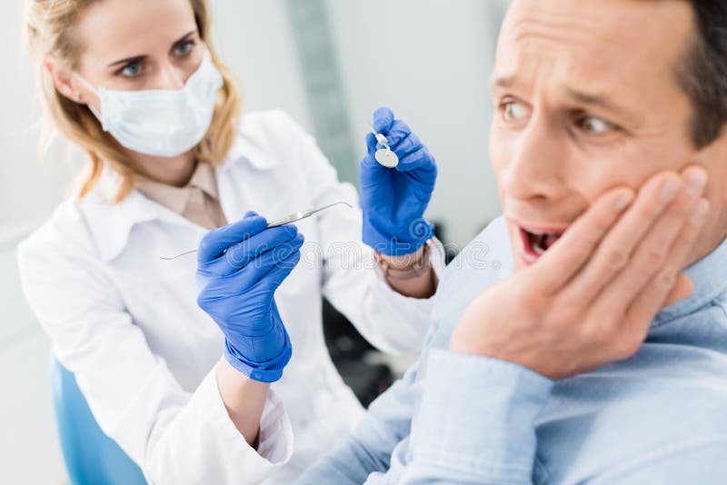 Il paziente maschio è impaurito del dentista in moderno fotografie stock Il paziente maschio è impaurito del dentista in moderno fotografie stock