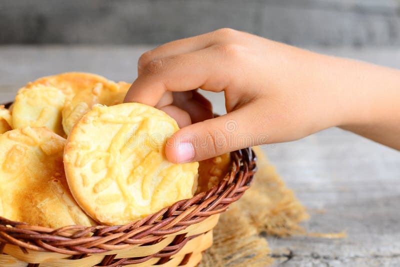 Il piccolo bambino prende un biscotto del formaggio da un canestro Imburri i biscotti del formaggio in un canestro di vimini su u immagini stock libere da diritti Il piccolo bambino prende un biscotto del formaggio da un canestro Imburri i biscotti del formaggio in un canestro di vimini su u immagini stock libere da diritti