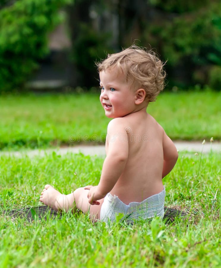 Il piccolo bambino riccio sta sedendosi sull'erba verde immagini stock Il piccolo bambino riccio sta sedendosi sull'erba verde immagini stock