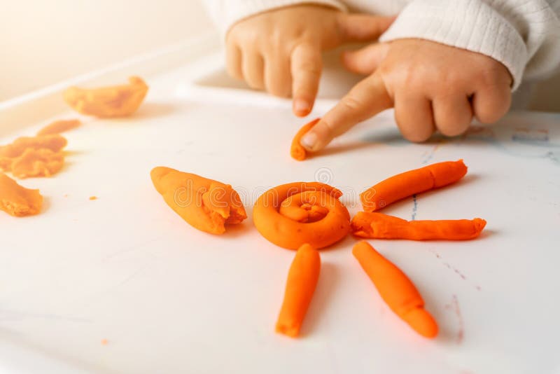 Il piccolo bambino riproduce la pasta del gioco. Modellazione del sole arancione. Immaginazione della creatività
