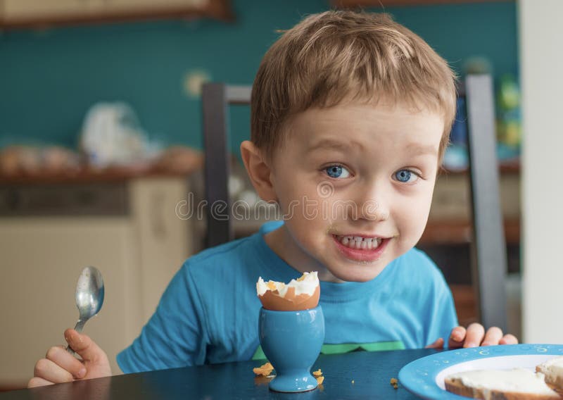 Il piccolo ragazzo di tre anni felice mangia un uovo immagine stock Il piccolo ragazzo di tre anni felice mangia un uovo immagine stock