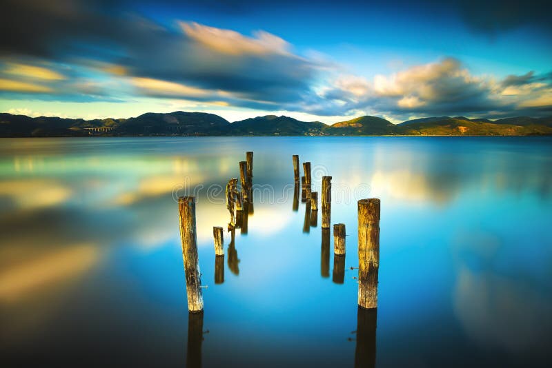 Il pilastro o il molo di legno rimane su un refle blu del tramonto e del cielo del lago