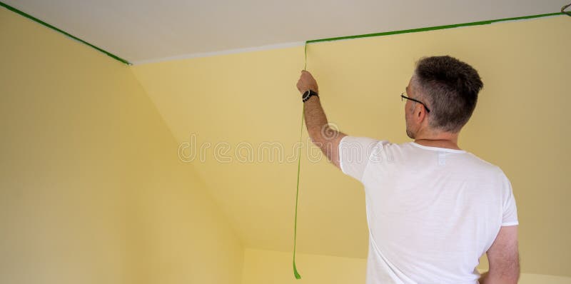 Painter removes masking tape and creates a sharp border between a yellow and white painted part of a wall. Painter removes masking tape and creates a sharp border between a yellow and white painted part of a wall.