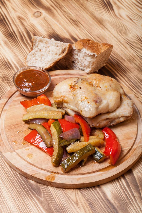 Il pollo con le verdure è servito sul tagliere rotondo sul bruciato su fotografia stock libera da diritti Il pollo con le verdure è servito sul tagliere rotondo sul bruciato su fotografia stock libera da diritti