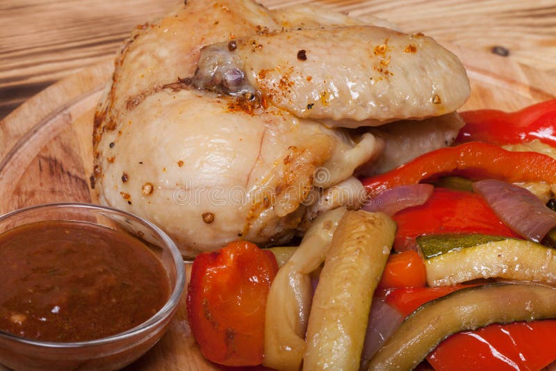 Il pollo con le verdure è servito sul tagliere rotondo sul bruciato su fotografia stock Il pollo con le verdure è servito sul tagliere rotondo sul bruciato su fotografia stock
