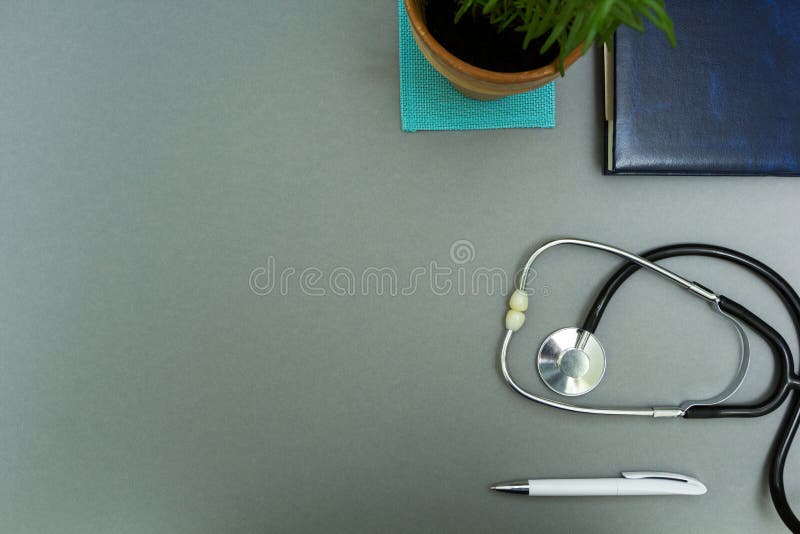Il posto di lavoro del medico Blocco note con la penna, lo stetoscopio ed il vaso da fiori su un fondo grigio fotografia stock Il posto di lavoro del medico Blocco note con la penna, lo stetoscopio ed il vaso da fiori su un fondo grigio fotografia stock