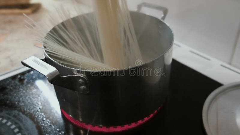 Il primo piano degli spaghetti del riso cade in un vaso di acqua calda sulla stufa Vista laterale