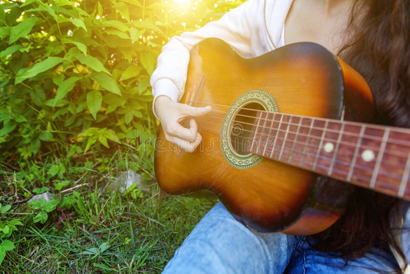 Il primo piano della donna passa il gioco della chitarra acustica sul fondo del giardino o del parco Ragazza teenager che impara fotografie stock libere da diritti Il primo piano della donna passa il gioco della chitarra acustica sul fondo del giardino o del parco Ragazza teenager che impara fotografie stock libere da diritti
