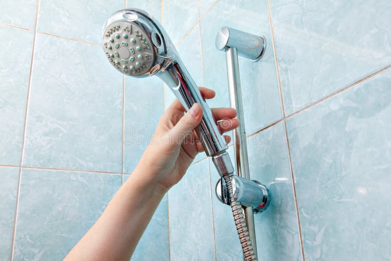 Replacing the plumbing in the bathroom, close-up wall mounted hand shower and hose holder with height adjustable bar slider rail, human hand holding a shower head. Replacing the plumbing in the bathroom, close-up wall mounted hand shower and hose holder with height adjustable bar slider rail, human hand holding a shower head.