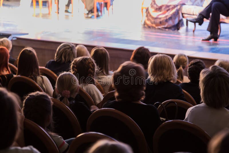 Il pubblico nel teatro che guarda un gioco Il pubblico nel corridoio: adulti e bambini immagini stock Il pubblico nel teatro che guarda un gioco Il pubblico nel corridoio: adulti e bambini immagini stock