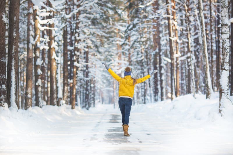 Il punto di vista posteriore della giovane donna in vestiti luminosi cammina su una strada in una foresta dell'inverno immagini stock Il punto di vista posteriore della giovane donna in vestiti luminosi cammina su una strada in una foresta dell'inverno immagini stock