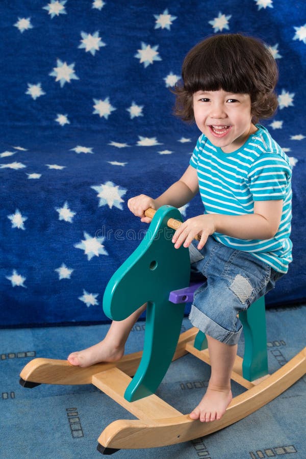 Il ragazzino sorridente si diverte su un cavallo del giocattolo fotografie stock Il ragazzino sorridente si diverte su un cavallo del giocattolo fotografie stock
