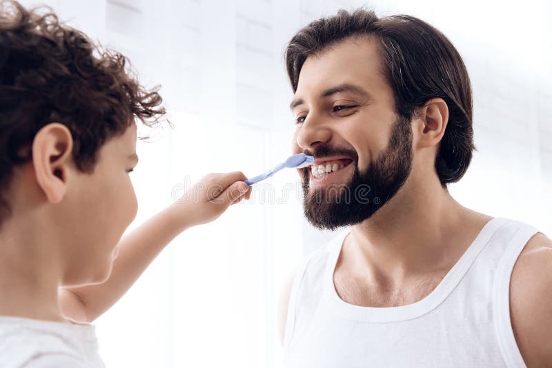 Il ragazzino sta pulendo i denti dell'uomo barbuto con lo spazzolino da denti immagine stock libera da diritti Il ragazzino sta pulendo i denti dell'uomo barbuto con lo spazzolino da denti immagine stock libera da diritti