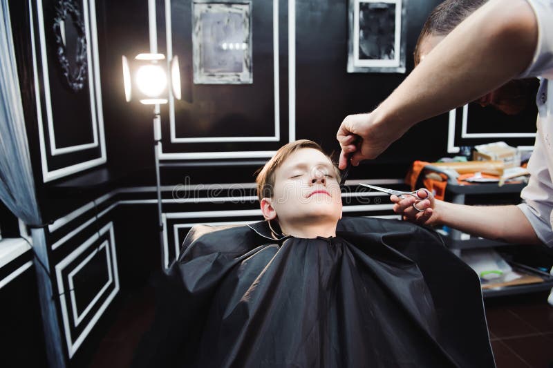 Il ragazzino sveglio sta ottenendo il taglio di capelli dal parrucchiere al parrucchiere fotografie stock libere da diritti Il ragazzino sveglio sta ottenendo il taglio di capelli dal parrucchiere al parrucchiere fotografie stock libere da diritti