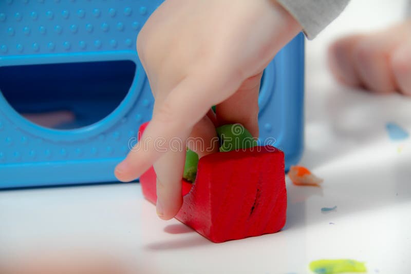 Il ragazzino tre anni si siede sulla tavola ed i giochi con plasticine e giocattoli, cubi e dadi di legno e di plastica immagine stock libera da diritti Il ragazzino tre anni si siede sulla tavola ed i giochi con plasticine e giocattoli, cubi e dadi di legno e di plastica immagine stock libera da diritti