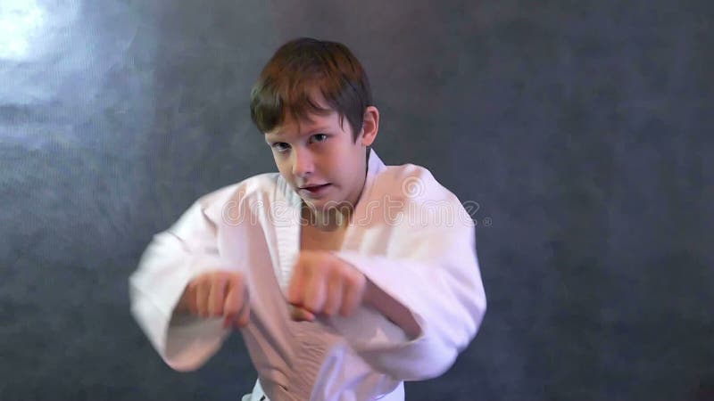 Il ragazzo adolescente di karatè nella lotta del kimono passa il movimento lento d'ondeggiamento dei pugni