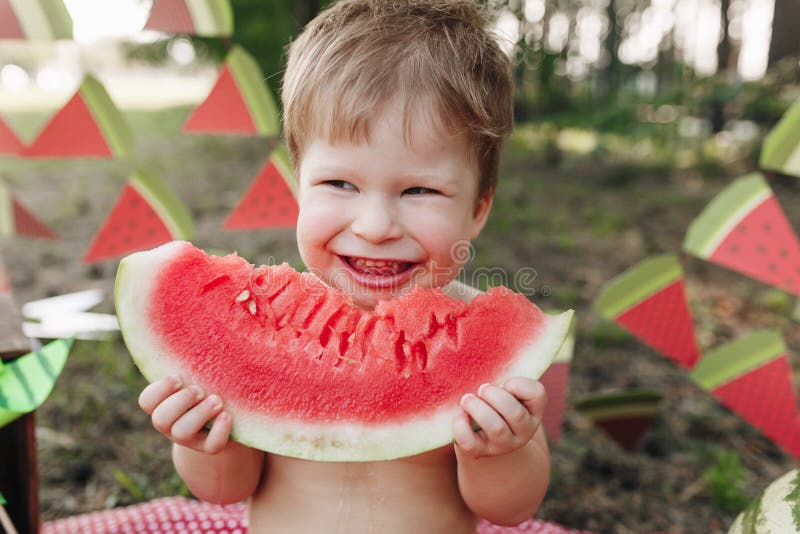 Il ragazzo biondo del bambino mangia l'anguria ed il sorriso Il bambino ha abitudini alimentari sane immagine stock