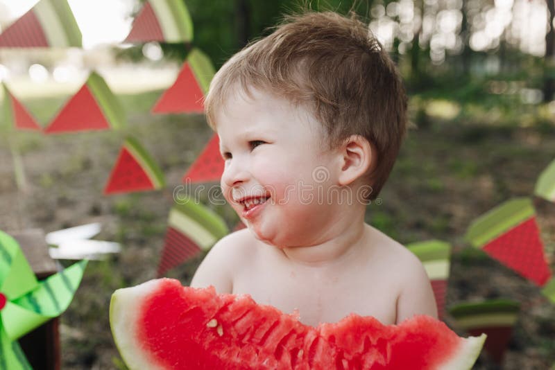 Il ragazzo biondo del bambino mangia l'anguria ed il sorriso Il bambino ha abitudini alimentari sane immagine stock