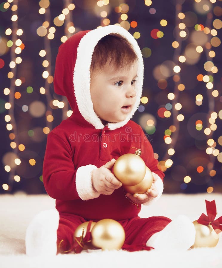 Il ragazzo del piccolo bambino vestito come Santa che gioca con la decorazione di natale, il fondo scuro con l'illuminazione e il fotografie stock libere da diritti Il ragazzo del piccolo bambino vestito come Santa che gioca con la decorazione di natale, il fondo scuro con l'illuminazione e il fotografie stock libere da diritti