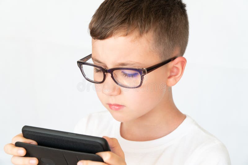 Il ragazzo di scuola sembra il video bello dello smartphone, in vetri immagini stock Il ragazzo di scuola sembra il video bello dello smartphone, in vetri immagini stock