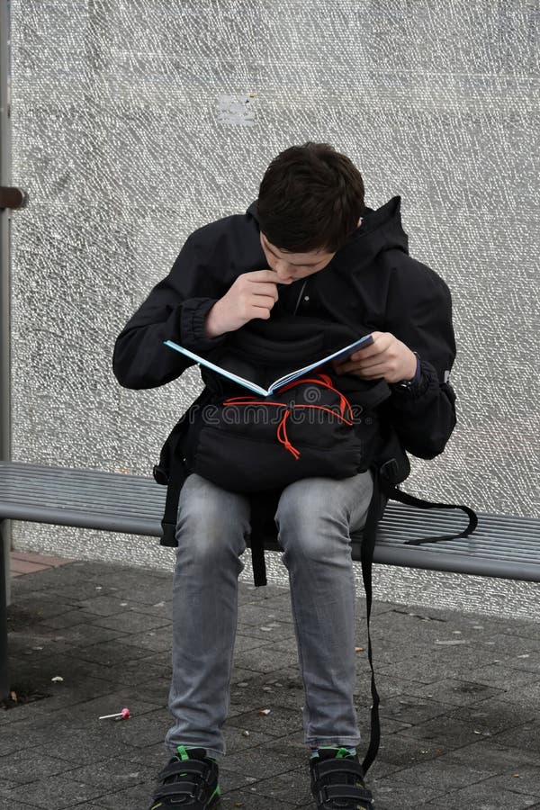 Il ragazzo fa il compito della scuola alla fermata dell'autobus, lui impara i vocables fotografia stock libera da diritti Il ragazzo fa il compito della scuola alla fermata dell'autobus, lui impara i vocables fotografia stock libera da diritti