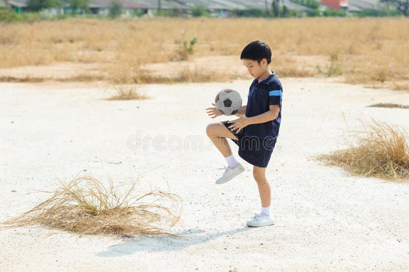 Il ragazzo gioca a calcio sulla terra del suolo asciutto fotografia stock Il ragazzo gioca a calcio sulla terra del suolo asciutto fotografia stock