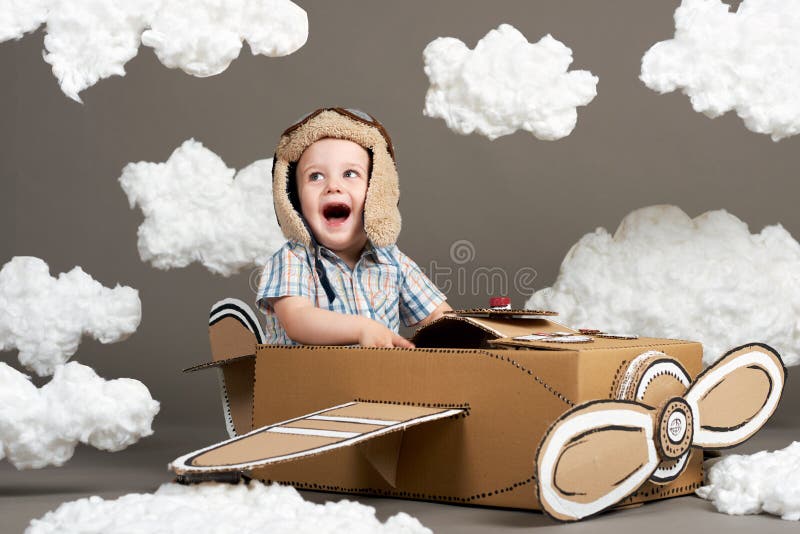 Il ragazzo gioca in un aeroplano fatto della scatola di cartone e dei sogni di diventare un pilota, nuvole da ovatta su un fondo