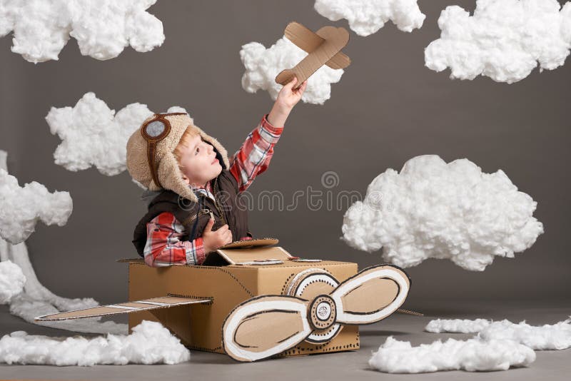 Il ragazzo gioca in un aeroplano fatto della scatola di cartone e dei sogni di diventare un pilota, nuvole di ovatta su un fondo