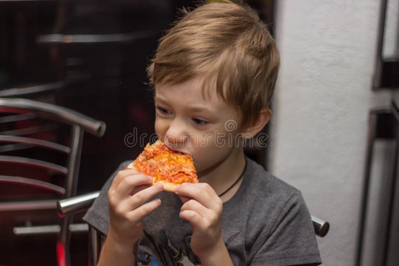 Il ragazzo mangia una pizza molto saporita con grande piacere fotografia stock libera da diritti Il ragazzo mangia una pizza molto saporita con grande piacere fotografia stock libera da diritti