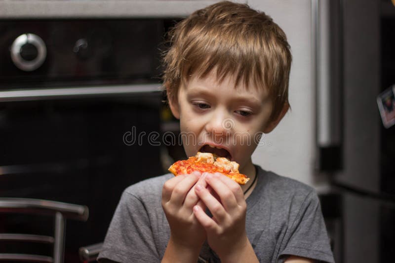 Il ragazzo mangia una pizza molto saporita con grande piacere immagine stock libera da diritti Il ragazzo mangia una pizza molto saporita con grande piacere immagine stock libera da diritti