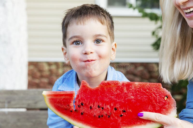 Il ragazzo ride e mangia un'anguria con sua madre nel giardino fotografia stock libera da diritti Il ragazzo ride e mangia un'anguria con sua madre nel giardino fotografia stock libera da diritti