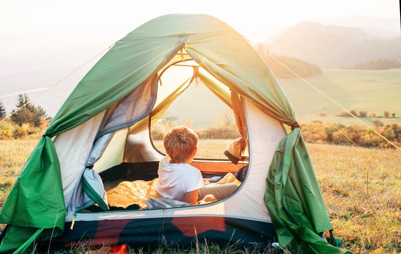 Il resto del ragazzo in tenda di campeggio e gode di con la luce del tramonto in valle della montagna