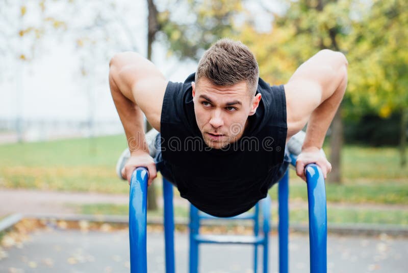 Il ritratto del giovane muscolare messo a fuoco nell'allenamento nero copre fare le immersioni sulle parallele simmetriche fotografie stock Il ritratto del giovane muscolare messo a fuoco nell'allenamento nero copre fare le immersioni sulle parallele simmetriche fotografie stock