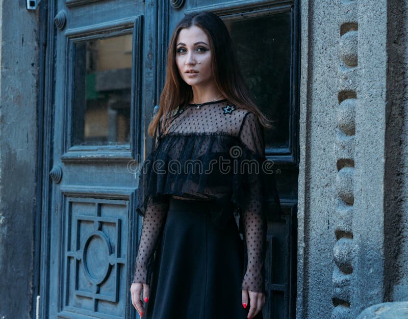 Il ritratto di bella ragazza, una ragazza castana in un vestito nero, supporti vicino ad una grande porta nera, entra in una nuo fotografia stock libera da diritti Il ritratto di bella ragazza, una ragazza castana in un vestito nero, supporti vicino ad una grande porta nera, entra in una nuo fotografia stock libera da diritti