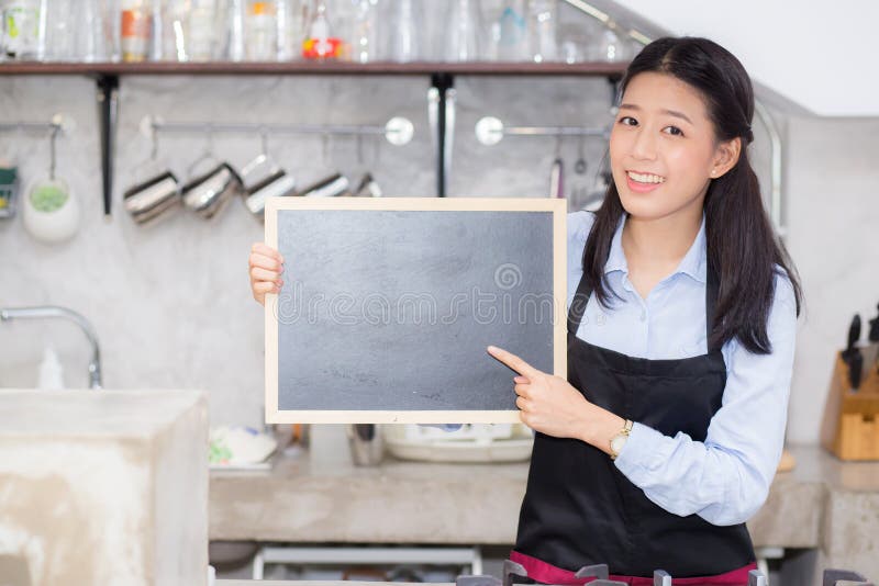 Il ritratto di bello giovane barista, donna asiatica è una lavagna diritta della tenuta degli impiegati immagini stock libere da diritti Il ritratto di bello giovane barista, donna asiatica è una lavagna diritta della tenuta degli impiegati immagini stock libere da diritti