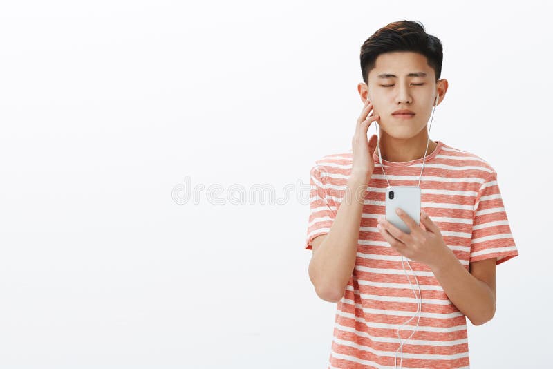 Il ritratto giovane del closing asiatico sveglio calmo e rilassato del tipo osserva premendo il earbud all'orecchio come piacere immagine stock libera da diritti