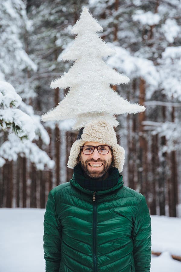 Il ritratto verticale dell'uomo barbuto allegro si diverte da solo nella foresta dell'inverno, tiene l'albero di abete artificial fotografia stock Il ritratto verticale dell'uomo barbuto allegro si diverte da solo nella foresta dell'inverno, tiene l'albero di abete artificial fotografia stock